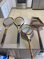 Four vintage wooden tennis racquets laid out on kitchen counter showing full frames, grips, and stringing patterns