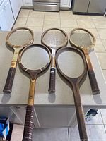 Five vintage wooden tennis racquets laid side by side showing their front with strings and grips.