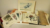 Assortment of Asian art prints and hanging scrolls laid out for display including botanical and landscape imagery.