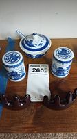 Overview of the porcelain lidded bowl with spoon, two lidded containers, and two wooden stands placed next to a measuring tape and lot number.