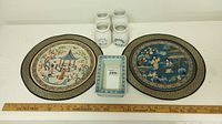 Overview of two crocks, two round placemats with Asian designs, and a small rectangular ceramic dish with blue floral border.