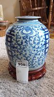 Full view of blue and white ceramic urn on wooden stand, showing floral and geometric patterns.