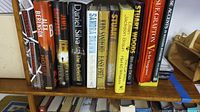 Books on shelf showing titles and authors including James Patterson, Sandra Brown, Daniel Silva.