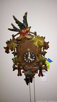 Front view of the vintage cuckoo clock showing the carved bird, leaves, and clock face with Roman numerals.