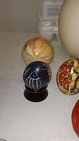 Several decorative eggs of different materials and colors, including a large ostrich egg, painted wood, stone, and metal eggs.