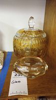 Photo showing large amber-colored etched glass bowl with lid and clear glass ashtray on a wooden surface