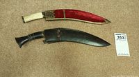 Two Sharps knives with distinct sheaths, one black leather with decoration, one red fabric with metal trim
