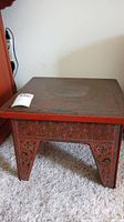 Side view of the small painted collapsible wooden table, showing red and black painted floral motif and carved designs on the leg and apron area.