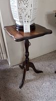 Wooden accent table showing scalloped square top with curved legs and dark finish
