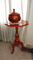 Full view of octagonal red painted wooden table with lidded bowl on top