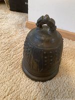 Photo showing bell shaped brass weight from an angle, highlighting decorative knobs and patina.