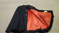 Interior of cape spread open showing orange satin lining and black wool outer edges.