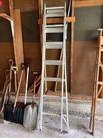 Full-ladder view showing the ladder in one of its standing configurations, alongside some snow shovels and garden tools.