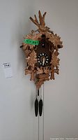Full view of carved wooden cuckoo clock mounted on wall, showing bird carving and leaf details, with measurement tag 11 x 23 inches
