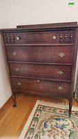 Front view of vintage wooden dresser showing four drawers, brass hardware, and carved spindle decoration on top drawer.