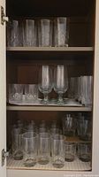 Top shelf with four crystal etched floral pattern tumblers and three clear tall cylinders with cut patterns