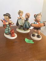 Wide angle showing all three Hummel figurines on wooden surface with a green marking labeled '5' nearby.