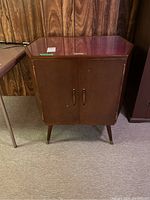 Mid Century Modern bar cabinet front view showing glass top, double doors, and tapered legs.