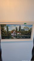 Front view of original framed painting depicting a duck pond with traditional German village houses and cathedral in the background.