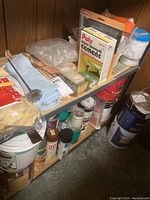 Shelf with a variety of painting and plaster supplies including cement, brushes, gloves, sandpaper, and plastic sheeting.