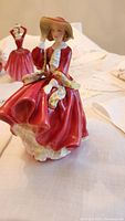 Close-up front angle of the Royal Doulton porcelain figurine showing lady in red dress with hat and sash.