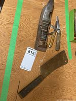 Photo of three knives: a large sheath knife with stacked handle and leather sheath, and two smaller vintage pocket knives with bone handles, one with serrated blade.