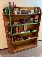 View of entire wooden shelf showing four shelves with green painted rails on three shelves and rounded edges.