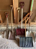 Photo showing six shovels including three metal gardening shovels, two snow shovels with plastic scoops, set against a wooden wall.