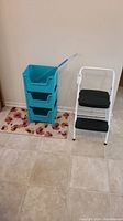 Photo showing white frame folding two-step stool with black steps alongside turquoise storage bins and tools.