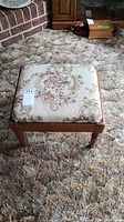 Top full view of vintage wooden foot stool showing floral brocade seat and wood frame.