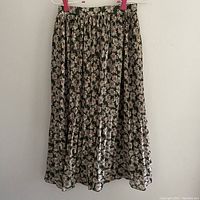 Black skirt with white and light pink daisy floral print, pleated, hung for display