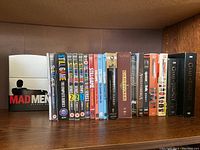 Shelf with multiple DVD box sets including Still Game (seasons 1–5 and complete series), Mad Men Season 1, Game of Thrones (seasons 1 and 2), and others.