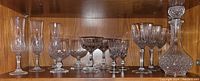 Shelved display of assorted crystal glasses including champagne flutes, snifter, cocktail coupes, wine goblets and a crystal decanter with stopper
