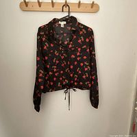 Black long-sleeve blouse with red floral print and drawstring hem on wooden hanger