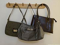 Three handbags hanging on wooden pegs: dark brown tote, gray shoulder bag, patterned shoulder bag with NR logo