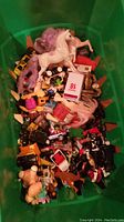 Top view of a green bin filled with assorted small toys including plastic horse figures, miniature vehicles, and small figures.