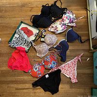 Photo of assorted large women's bathing suits including bikini tops and bottoms with various patterns and colors on a wooden floor.