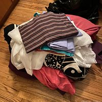 Pile of assorted folded fabrics in various colors and patterns on wooden floor