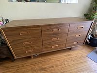 View of the full wooden buffet showing nine drawers arranged in three columns. It features a mid-century modern design with angled sides and cylindrical legs.