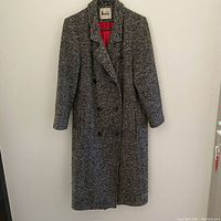 Full view of the Niccolini wool trench coat hanging on a wall, showing its length, double-breasted front, and black-white woven pattern.
