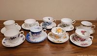 Front overview of 8 antique floral patterned cups and saucers in various colors and designs.