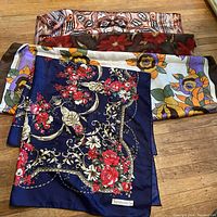 Top view showing four scarves laid out with floral and abstract designs, prominently featuring a navy blue scarf with red floral and ornamental pattern by Sunkyung Sa.