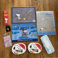 Photo displays two Snoopy metal lunchboxes with Universal Studios Japan branding, a translucent Snoopy pencil case, a plastic Snoopy pencil box, and various small Snoopy stationery items.