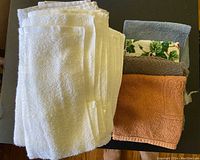 Photo showing eleven towels stacked with different colors including white, blue, floral patterned, dark gray and orange with embossed design.