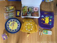 Displayed assortment of Pokemon items including backpacks, figures, cards, keychain watch, and accessories arranged on wooden floor.