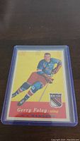 Front image of 1957-58 Topps Gerry Foley hockey card showing player in blue Rangers uniform on yellow background with card number 57.