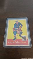 Front of 1957-58 Topps Larry Cahan hockey card sealed in a plastic protective holder, showing the player in uniform with details of team and position.