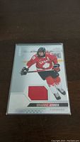 Front of Brianne Jenner hockey card with embedded red jersey piece, player name, and image in Team Canada hockey uniform.