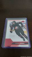 Front side of the Natalie Spooner hockey trading card showing her in Team Canada black uniform skating on ice.