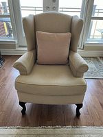 Front view of chair with accent pillow showing wingback backrest, rolled arms and cabriole legs